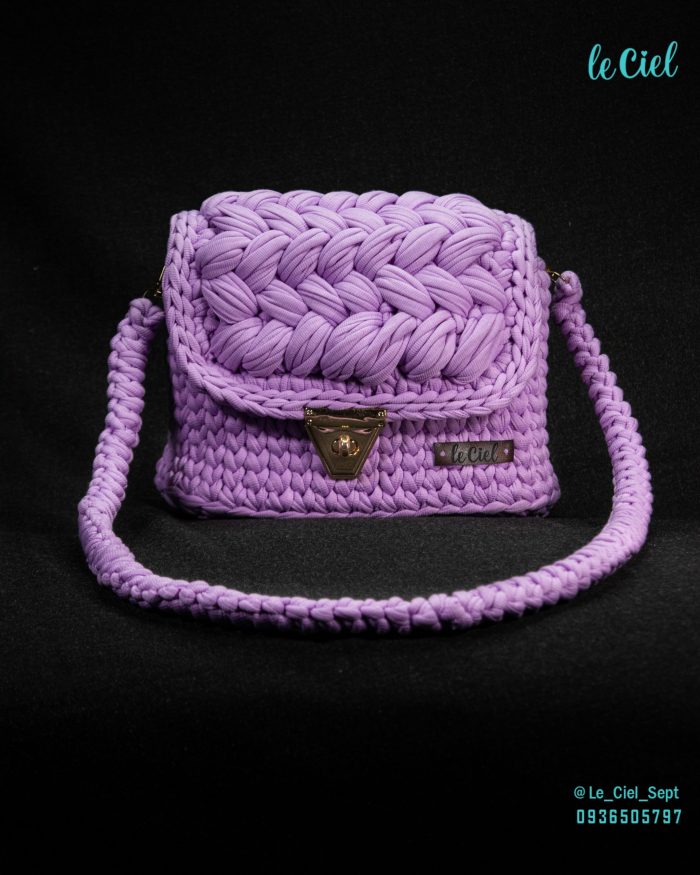 A handmade shoulder bag in a rich, deep shade of purple. The bag features a sturdy strap and a spacious main compartment, perfect for carrying daily essentials. The exterior is crafted from soft, supple leather, with a subtle texture that adds a touch of sophistication. The bag is adorned with intricate stitching and a simple, elegant design, making it a versatile accessory for any outfit.
