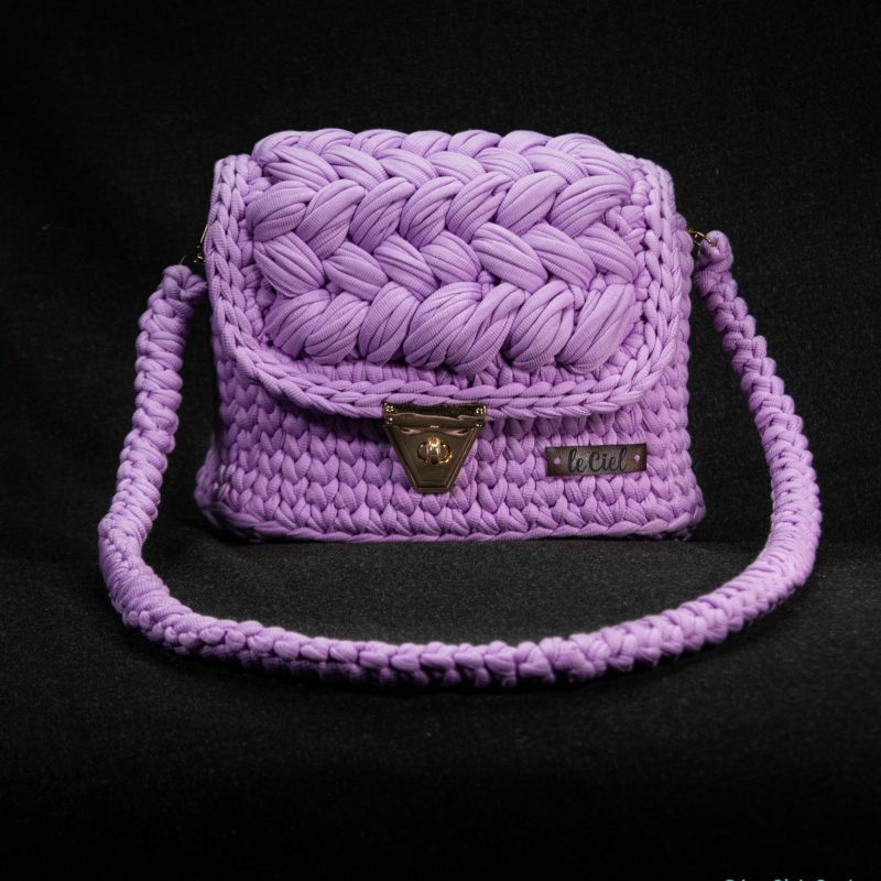 A handmade shoulder bag in a rich, deep shade of purple. The bag features a sturdy strap and a spacious main compartment, perfect for carrying daily essentials. The exterior is crafted from soft, supple leather, with a subtle texture that adds a touch of sophistication. The bag is adorned with intricate stitching and a simple, elegant design, making it a versatile accessory for any outfit.